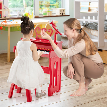 A mother kneels beside her daughter who is playing the red electronic piano keyboard