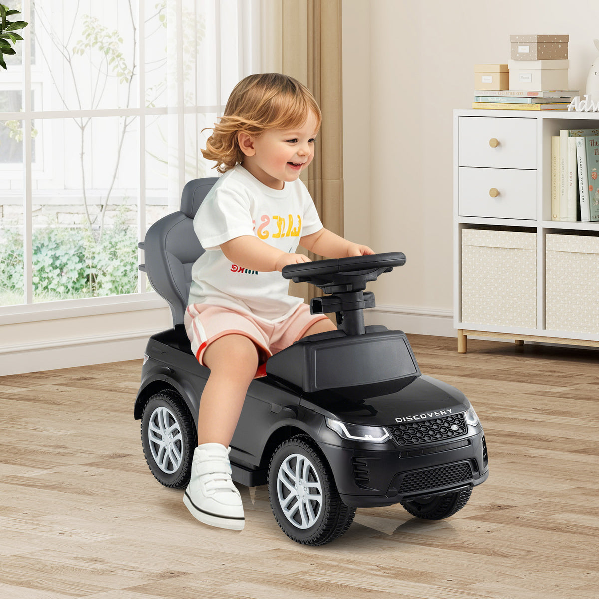 A toddler happily rides the black push and pedal ride on toy indoors