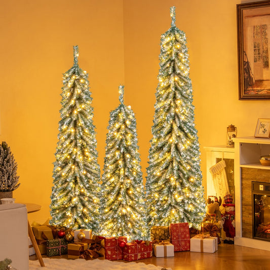 Three artificial Christmas trees with lights and snow decoration in a living room with presents