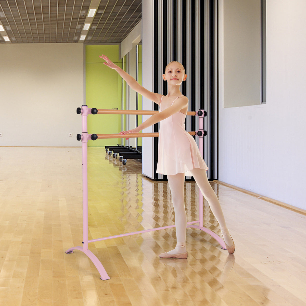 A young ballet dancer practices at the pink barre in a dance studio