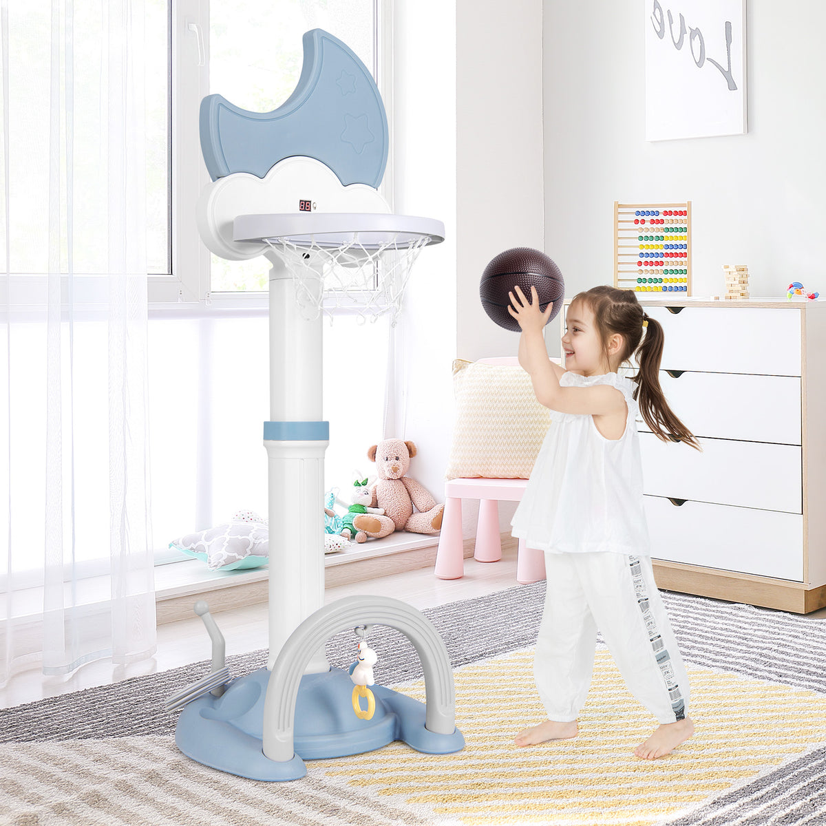 The blue kids basketball hoop with adjustable height, shown indoors with a girl playing basketball