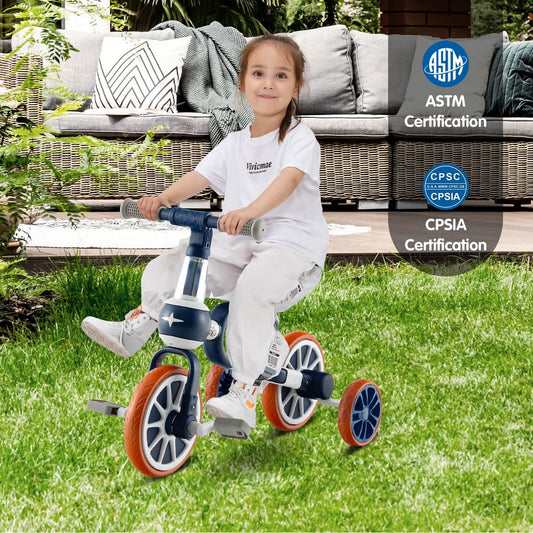 A young girl happily rides the navy training trike on a grassy lawn with outdoor furniture