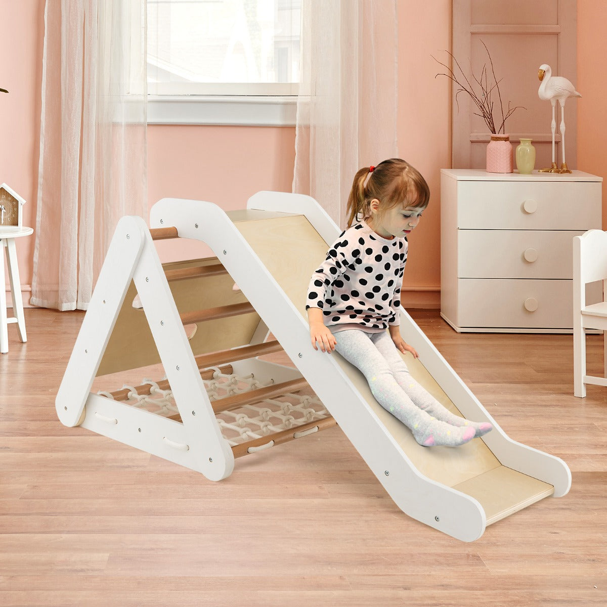 A young girl slides down the ramp of the wooden climbing frame in a child's bedroom