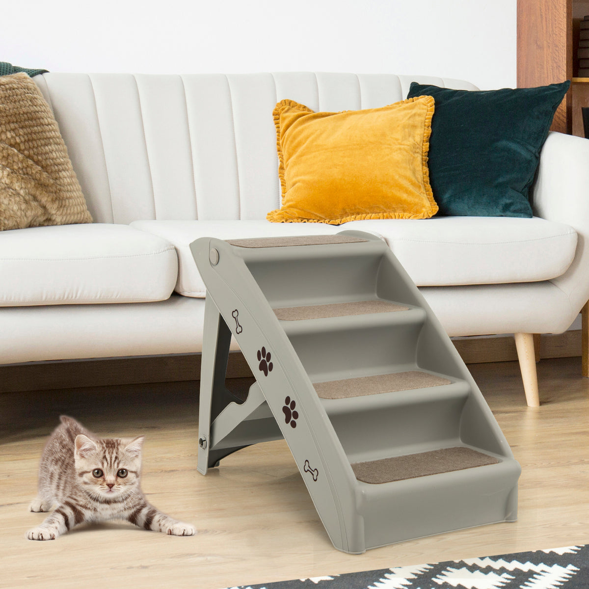 A grey pet stair unit is placed in front of a sofa, with a kitten sitting at the bottom