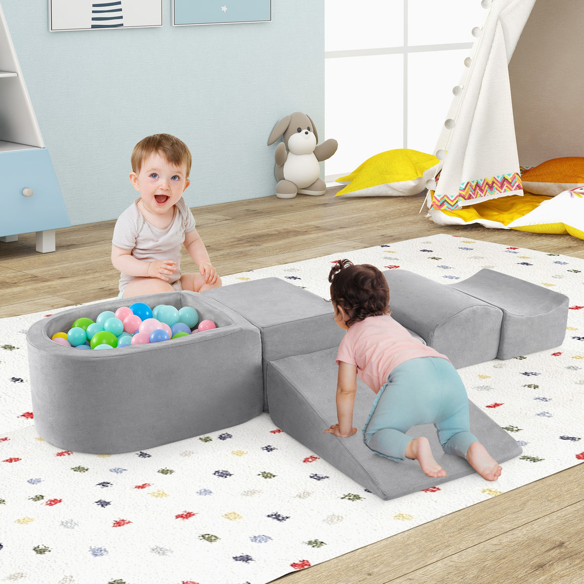 The soft play set arranged on a rug with two babies playing with the ball pit and ramp