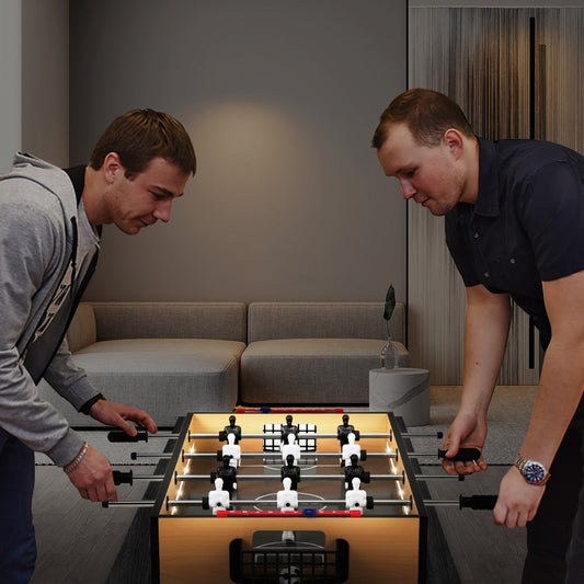 Two men playing a game of foosball on a table with LED lights in a modern room
