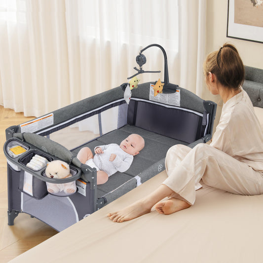 The travel cot with a baby lying inside and a woman sitting beside it