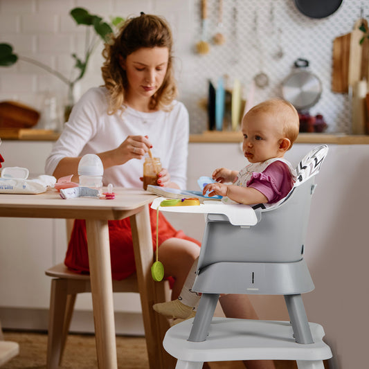 Mother feeding a baby in the high chair in a kitchen setting