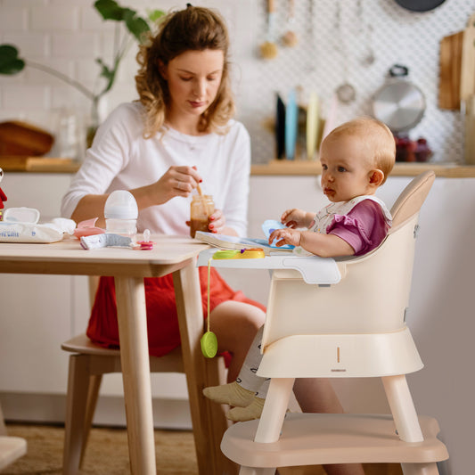 Mother feeding a baby in the high chair at a table