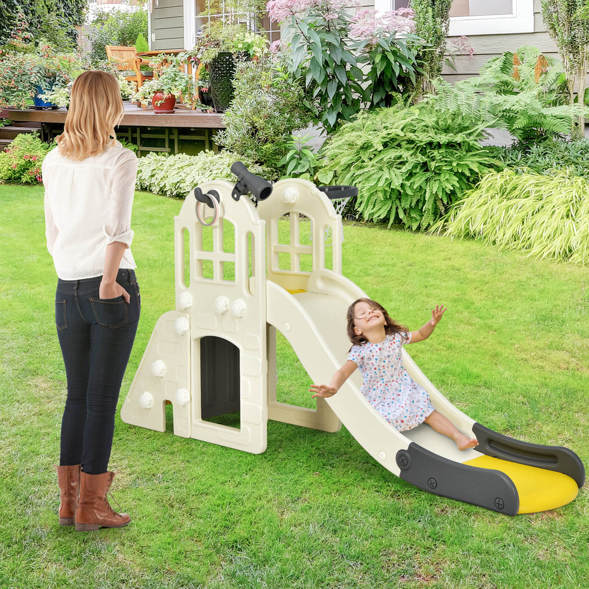 The kids slide set up on a green lawn with a child sliding down while a woman watches