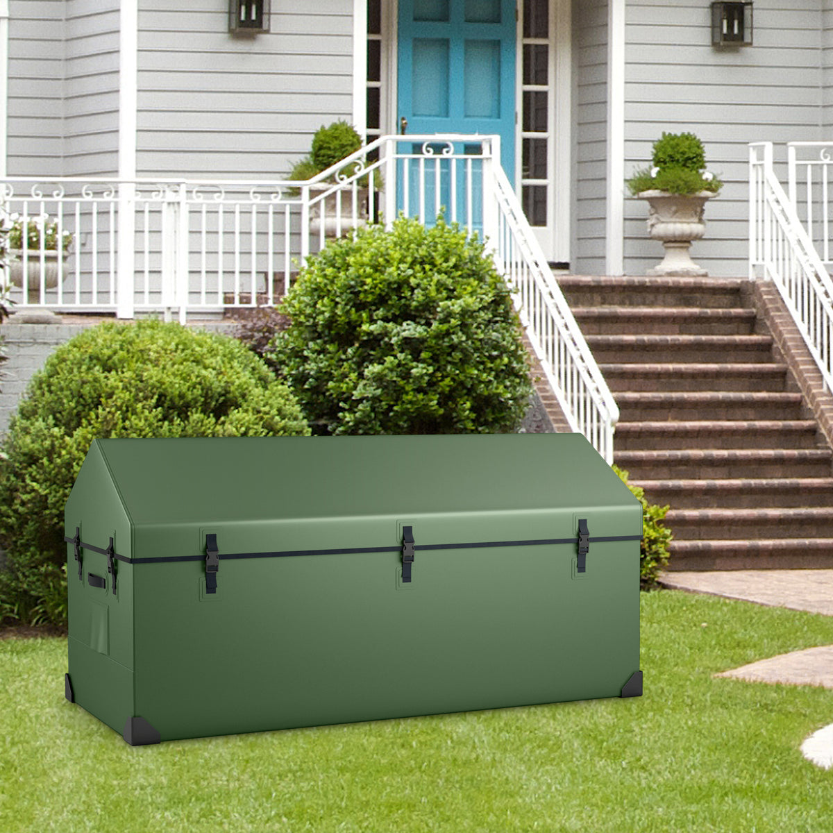 The green outdoor storage box with black clasps, sitting on a lawn in front of a house with steps and bushes