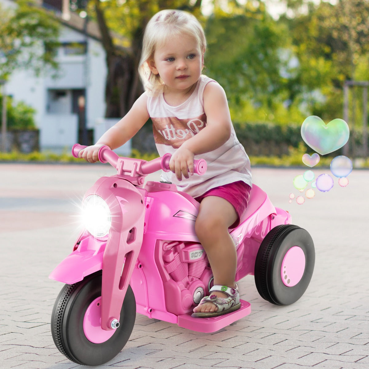 A young child happily riding the pink electric motorbike on a paved surface