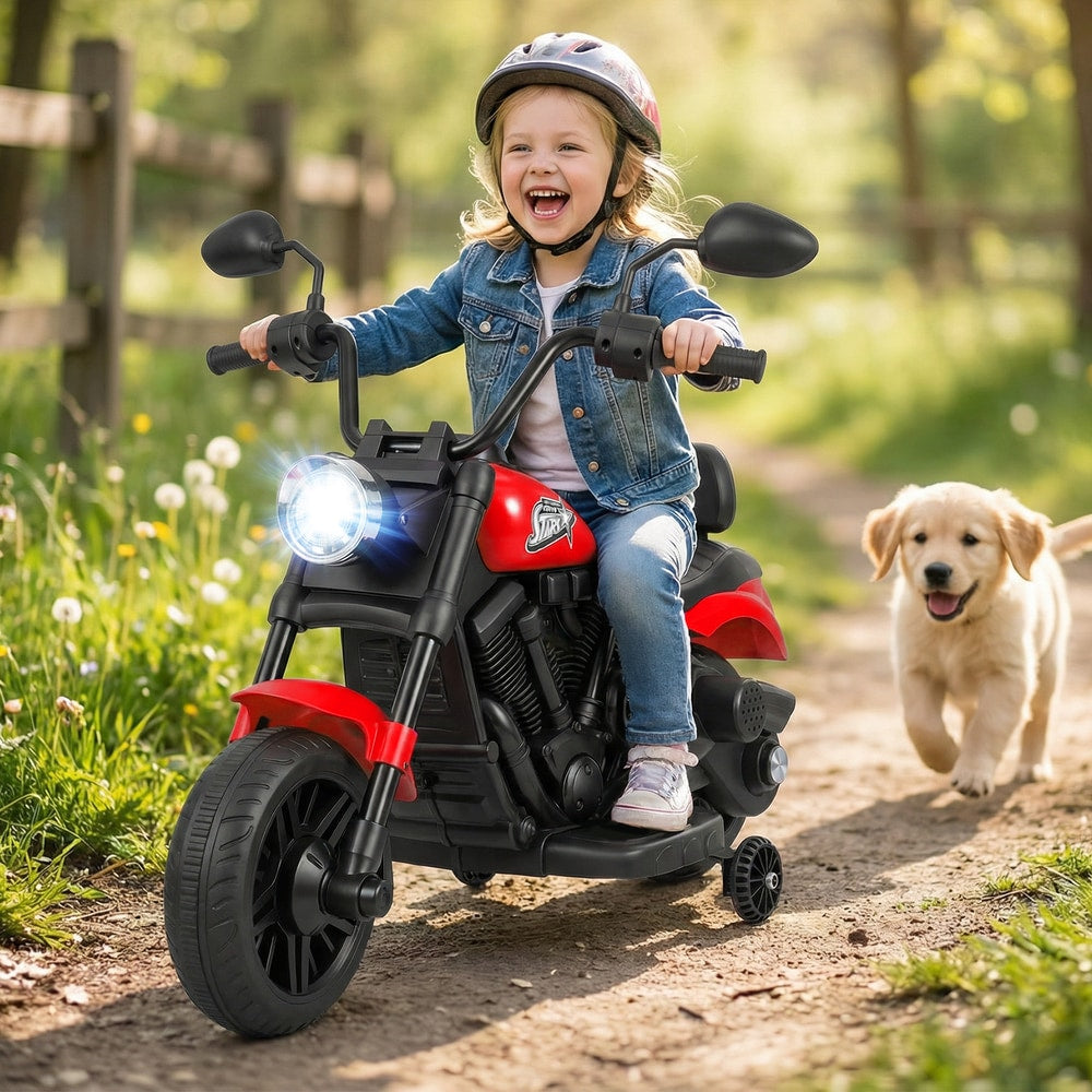 A young child rides the red kids electric motorbike outdoors with a puppy running alongside