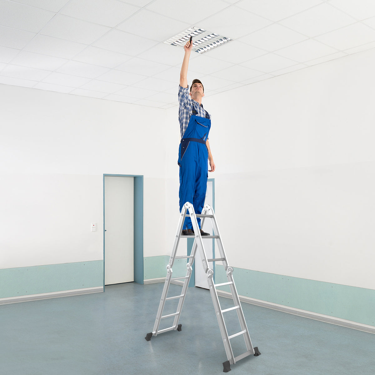 A man in a blue uniform using the extension ladder to change a ceiling light fitting