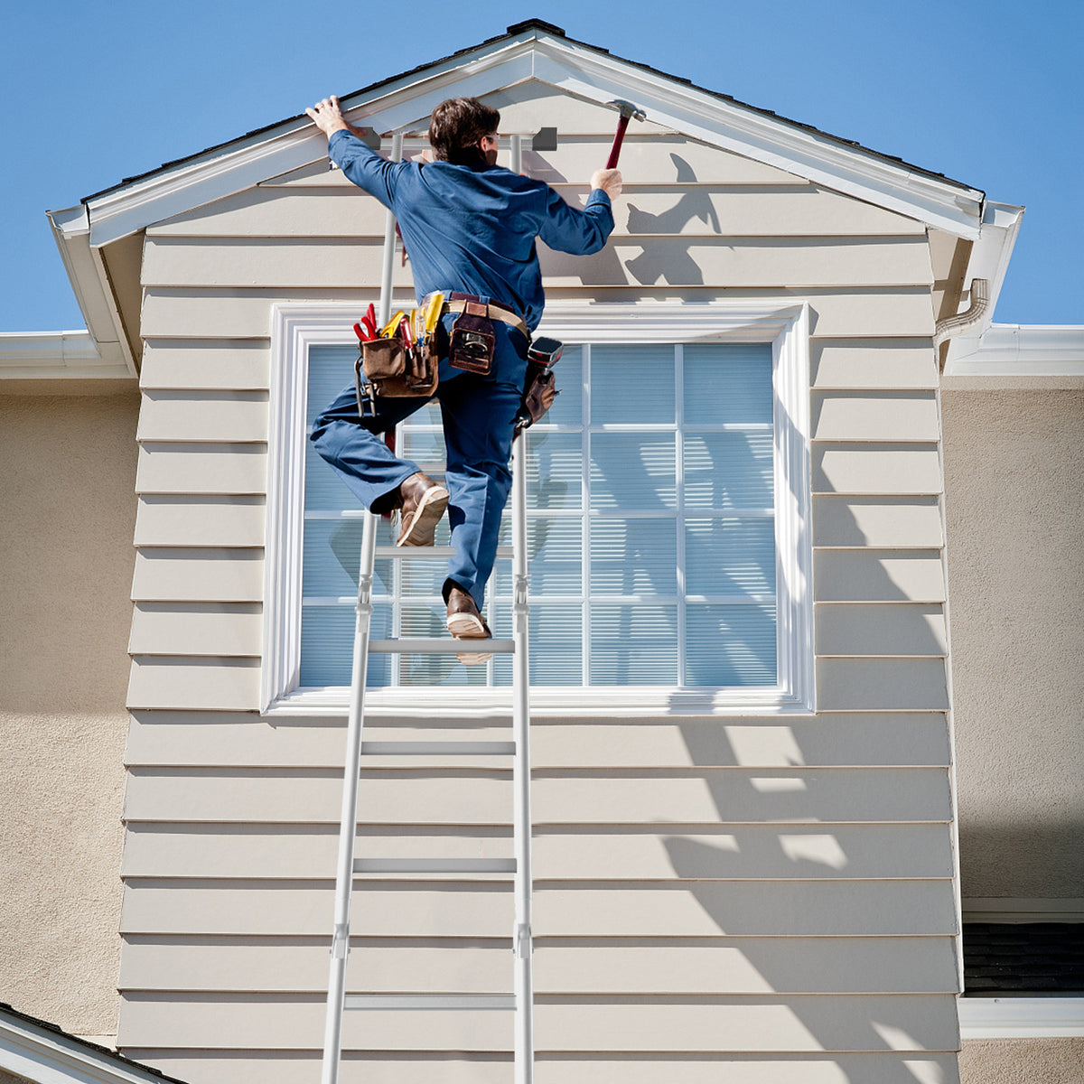 A man using the extension ladder to work on the exterior of a house