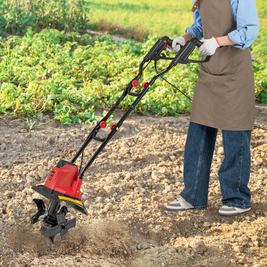 The garden tiller being used by a person in an apron to cultivate soil in a vegetable patch
