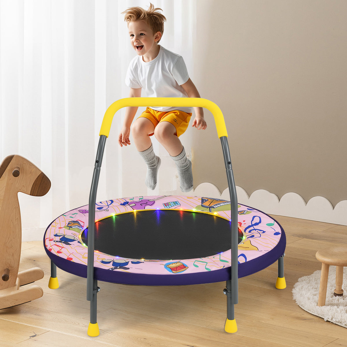 A young boy jumps on the pink folding mini trampoline with musical notes and LED lights, with a wooden rocking horse nearby
