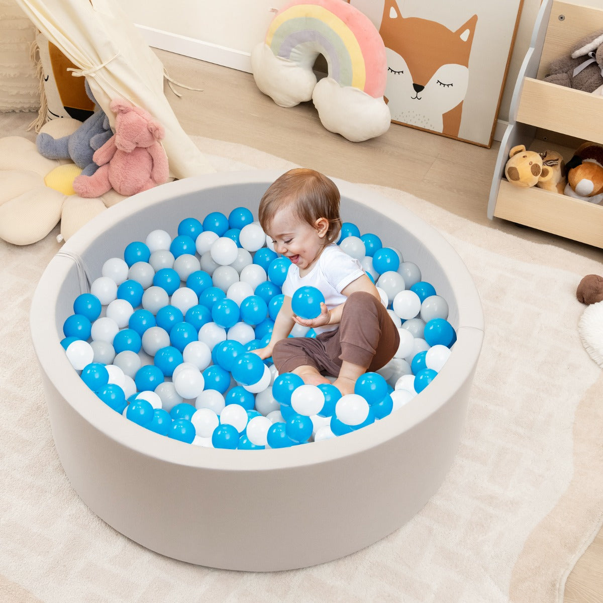 A baby playing in the soft play set with blue, white and grey balls