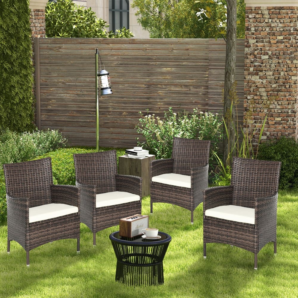 Four rattan chairs with cream cushions around a small black table in a garden setting