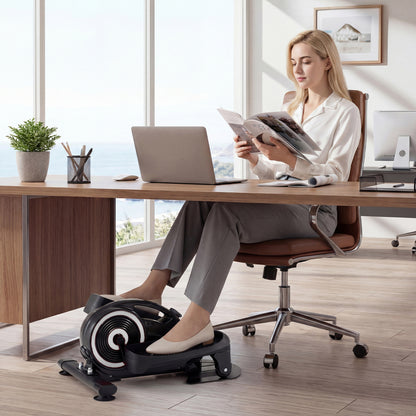 A woman using the under desk elliptical pedal exerciser while working at her desk