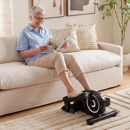 An older woman using the under desk elliptical pedal exerciser while relaxing on a sofa