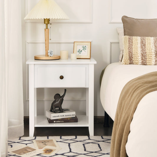 The white bedside table placed next to a bed with a lamp and decorative items on top