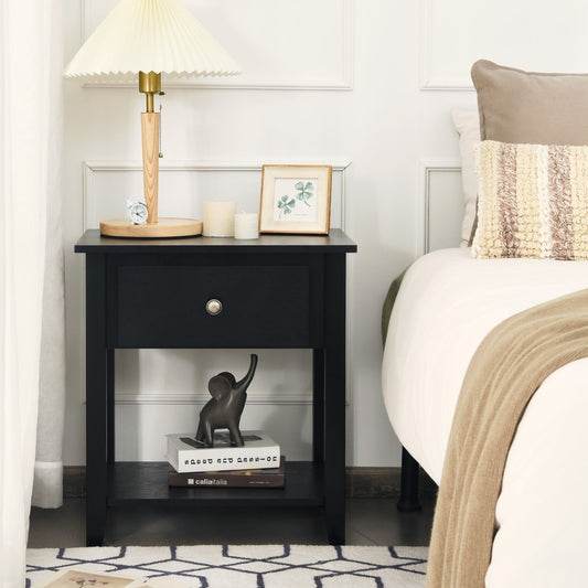 Black narrow side end table with drawer and shelf next to a bed with lamp and books