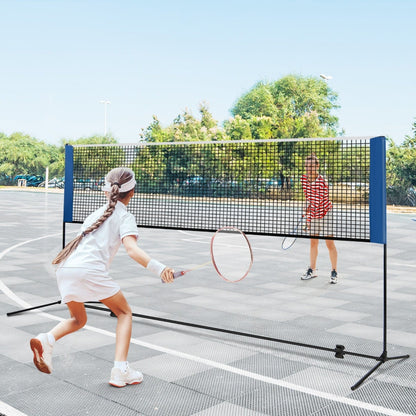 A portable badminton net set being used by people playing badminton on a paved court