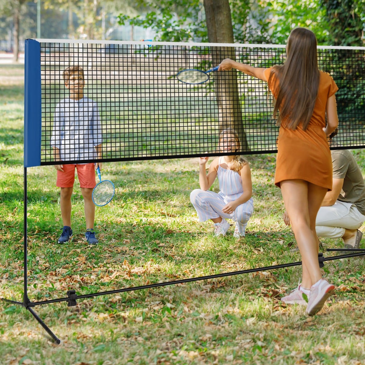A portable badminton net set being used by people playing badminton in a grassy garden