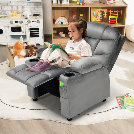 A young girl reads a book while sitting in the grey kids recliner chair in a playroom