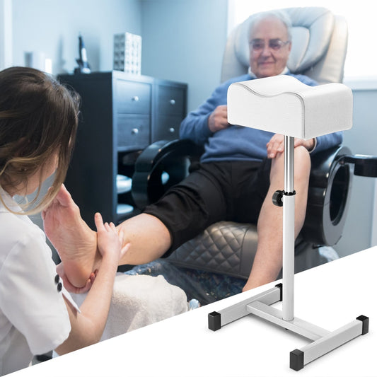 A white adjustable footrest is used by a therapist for a client's pedicure in a salon