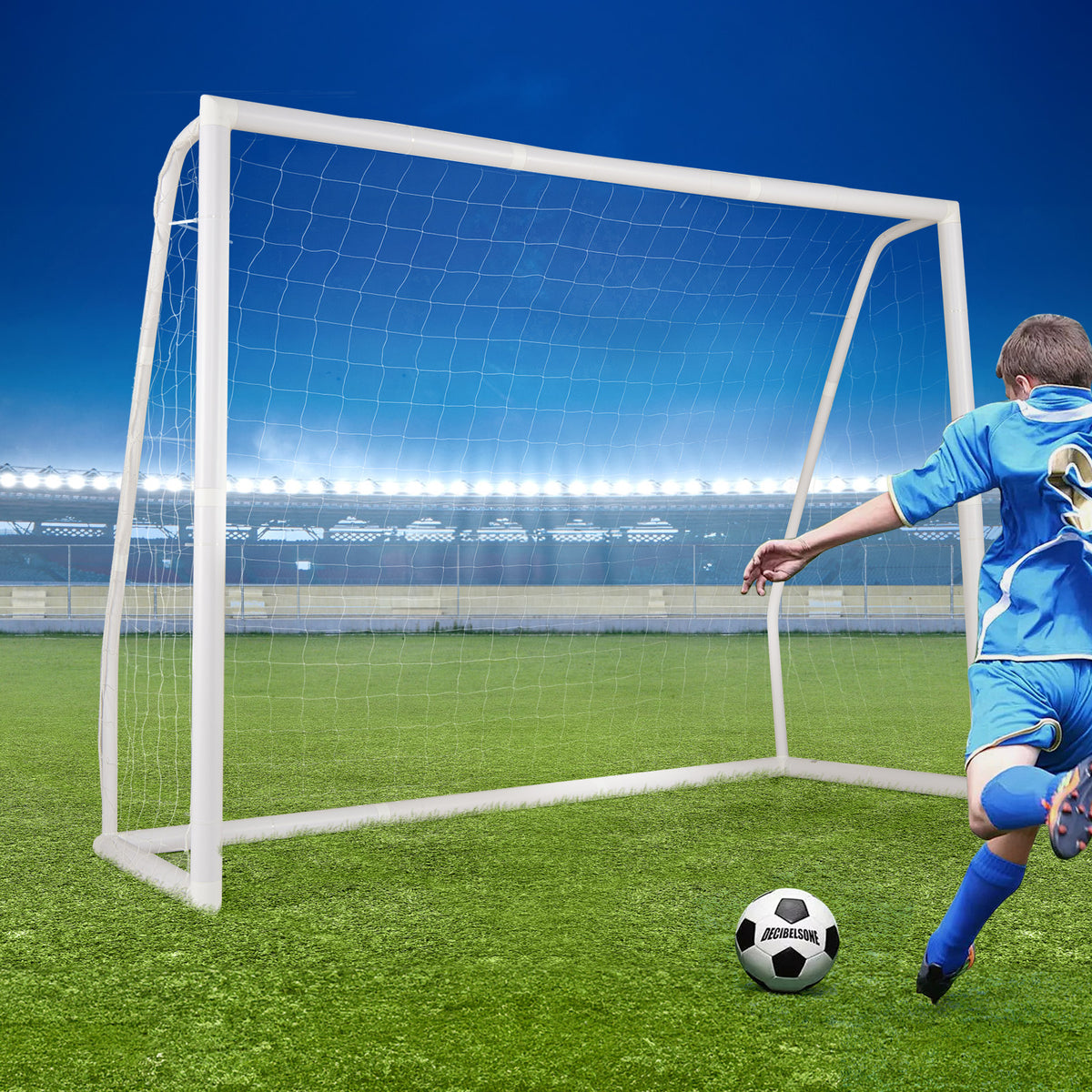 A boy kicks a football towards the soccer goal on a sports field at night