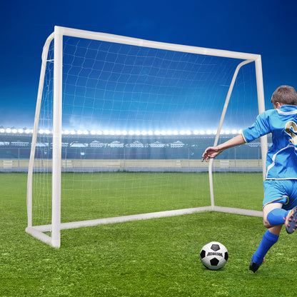 A boy kicks a football towards the soccer goal on a sports field at night