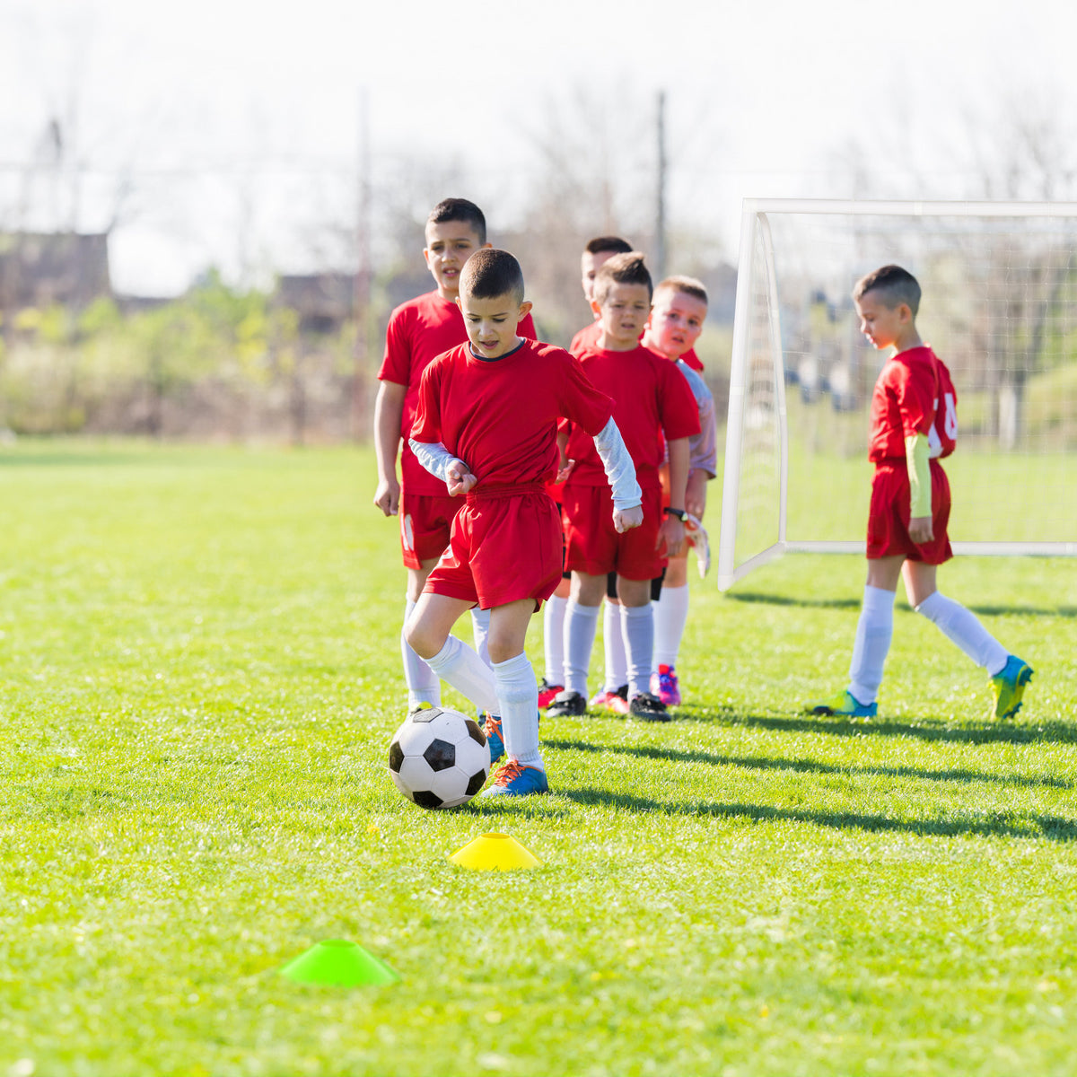 Children practice football drills using the soccer goal and cones