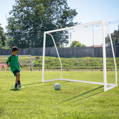 A boy plays football with the soccer goal set up on a grassy field