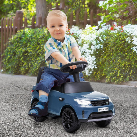 A young boy sitting on the light blue kids ride-on car on a paved path in a garden