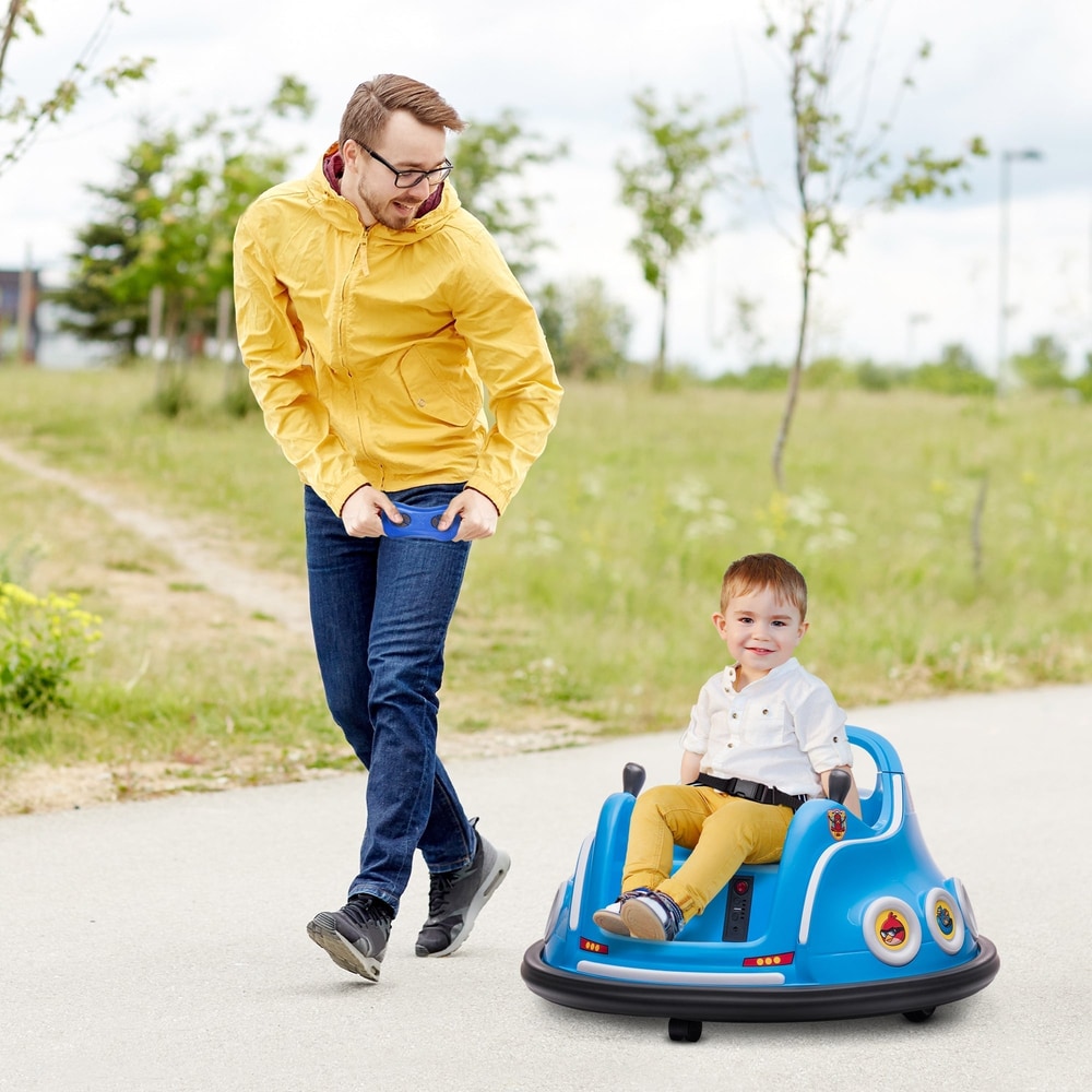 A father pushes his son on a blue kids electric bumper car in a park