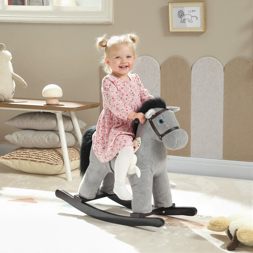 A smiling toddler girl rides the grey plush rocking horse in a brightly lit nursery room