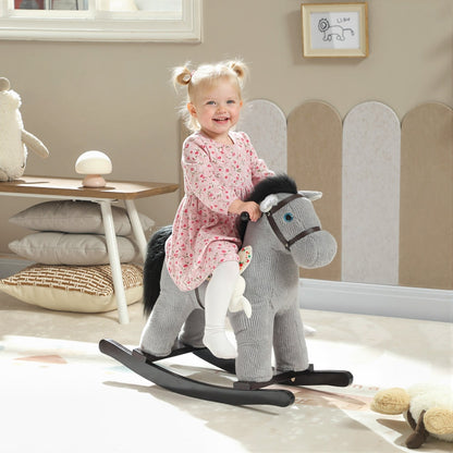 A smiling toddler girl rides the grey plush rocking horse in a brightly lit nursery room
