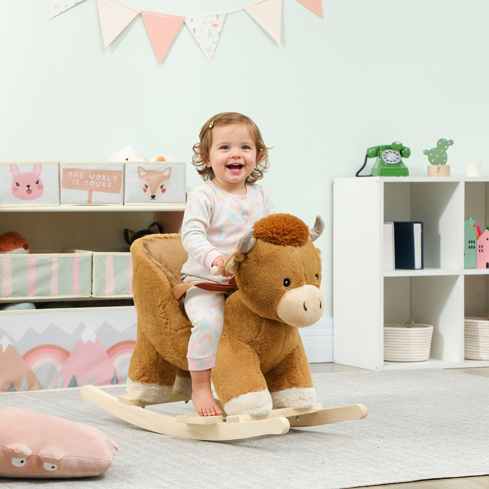 A happy toddler sits on the brown plush rocking cow in a child's playroom