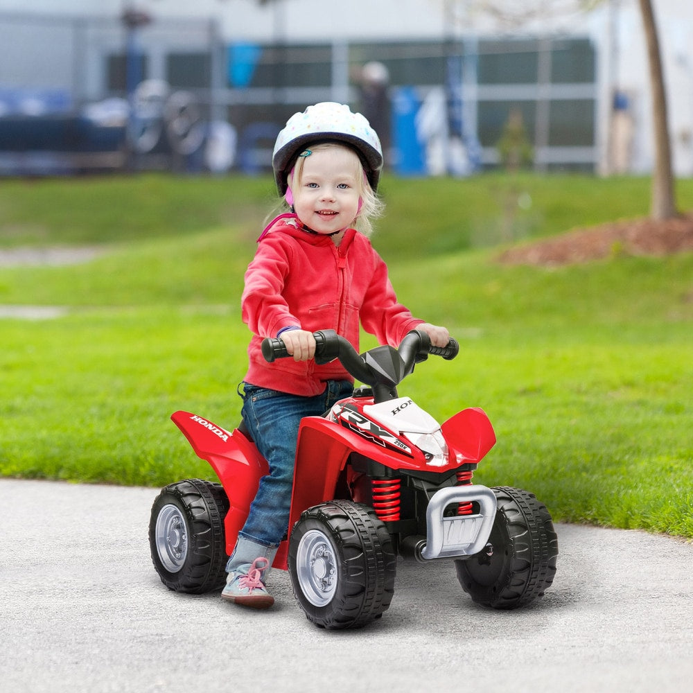A young child wearing a helmet riding the red electric quad bike on a paved path