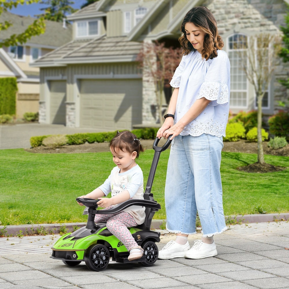 A toddler sits in the green ride-on car while a woman pushes it along a path
