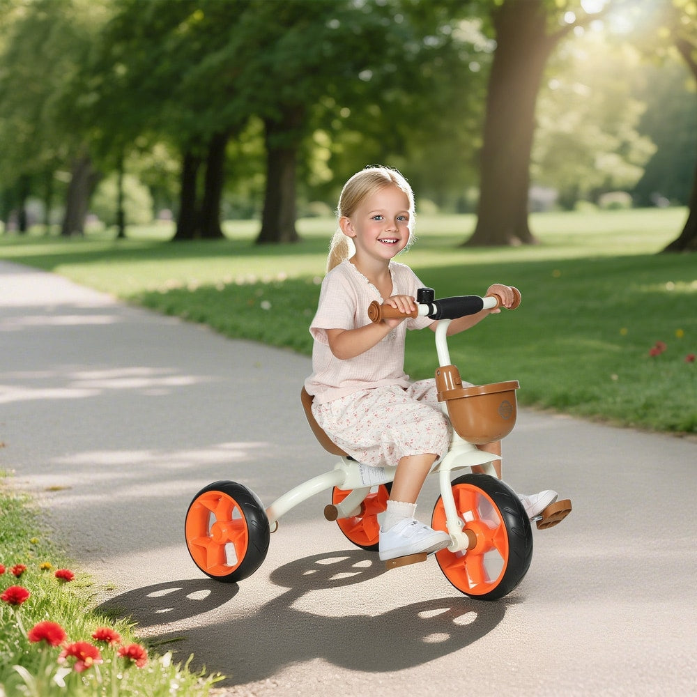 A happy young girl rides the orange kids tricycle on a paved path in a park