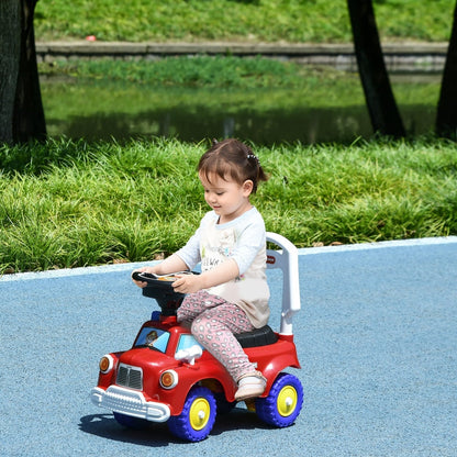 A young child sitting on the red ride-on fire truck on a blue path in a park