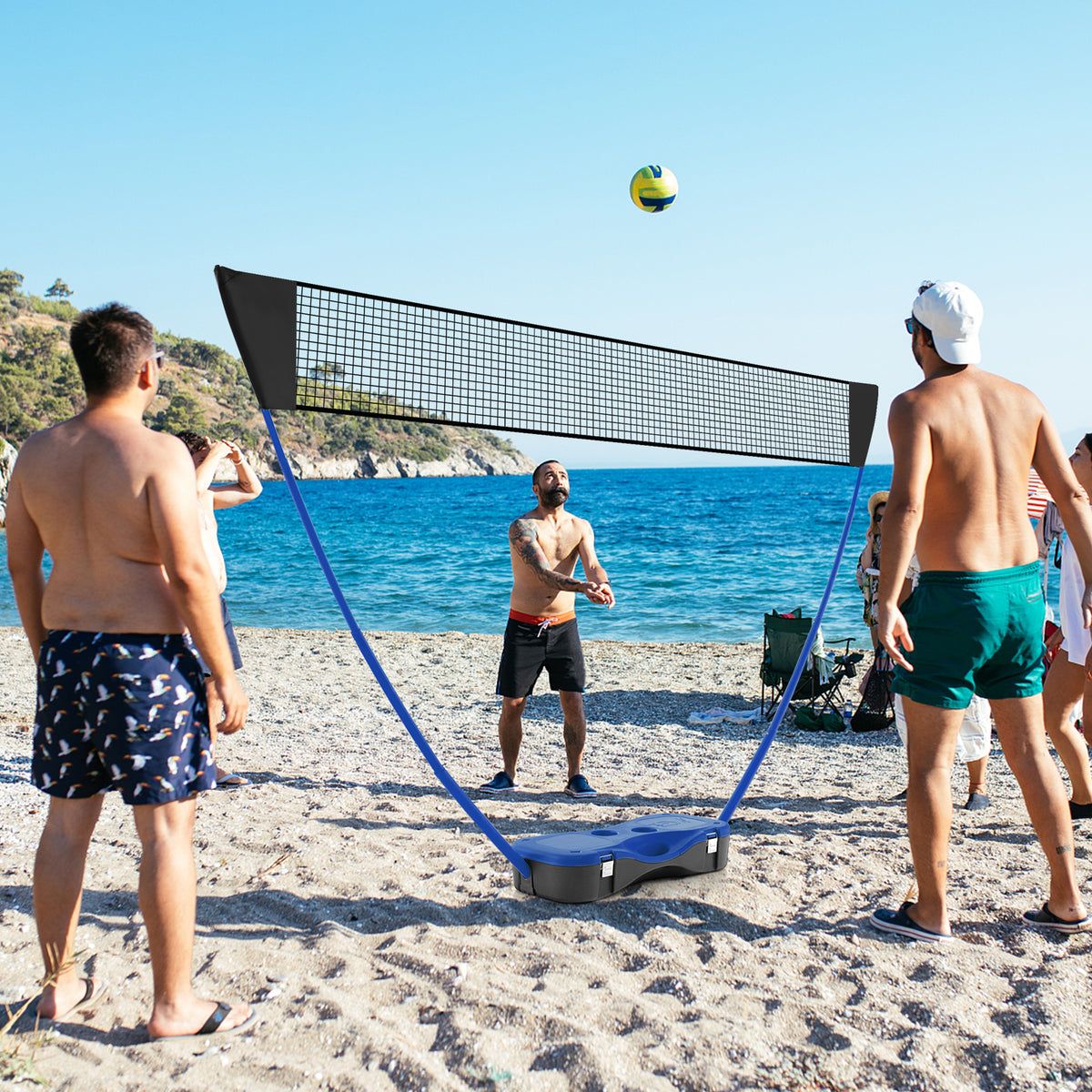 The portable badminton net set being used on a beach with adults playing volleyball