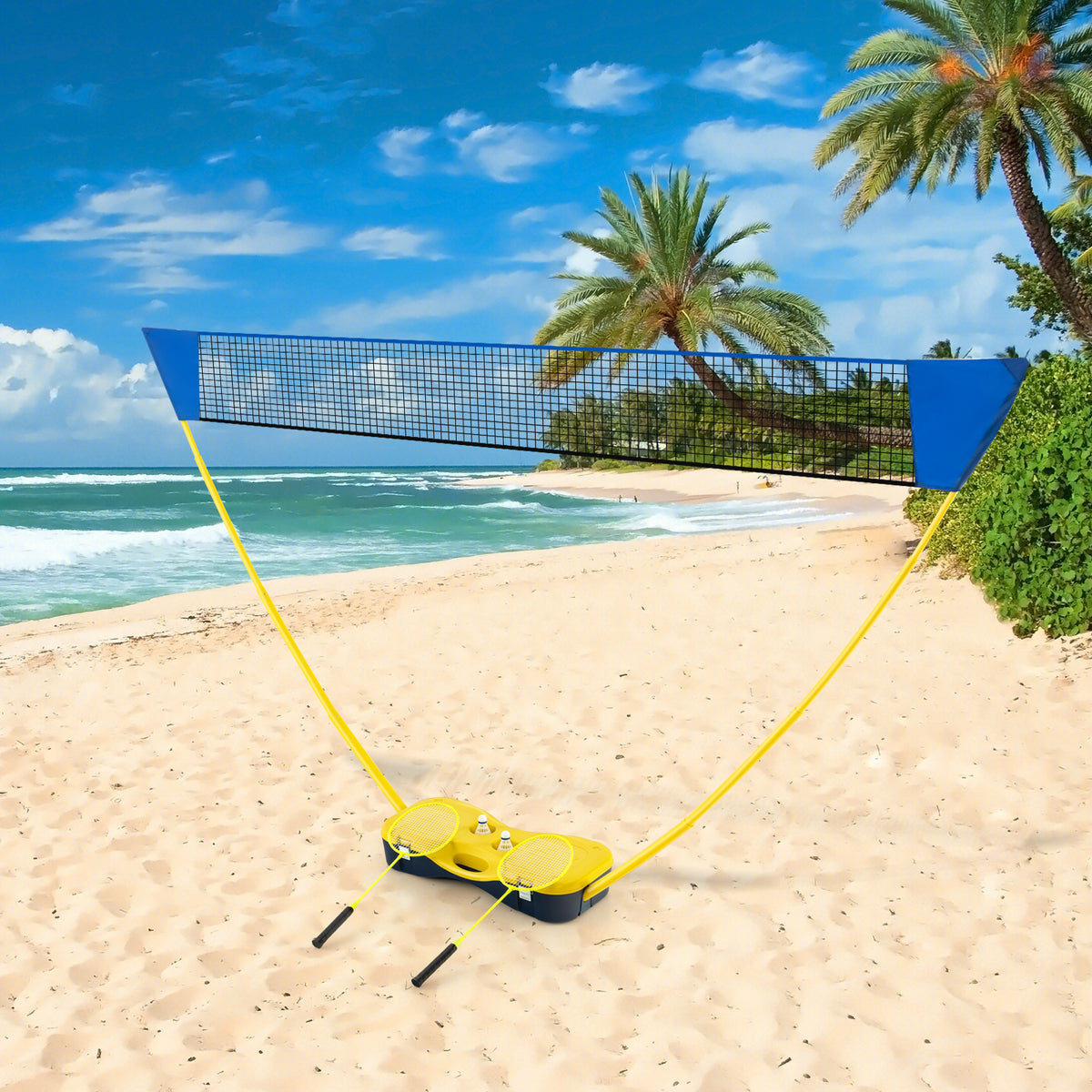 The portable badminton net set on a sandy beach with palm trees and the ocean in the background