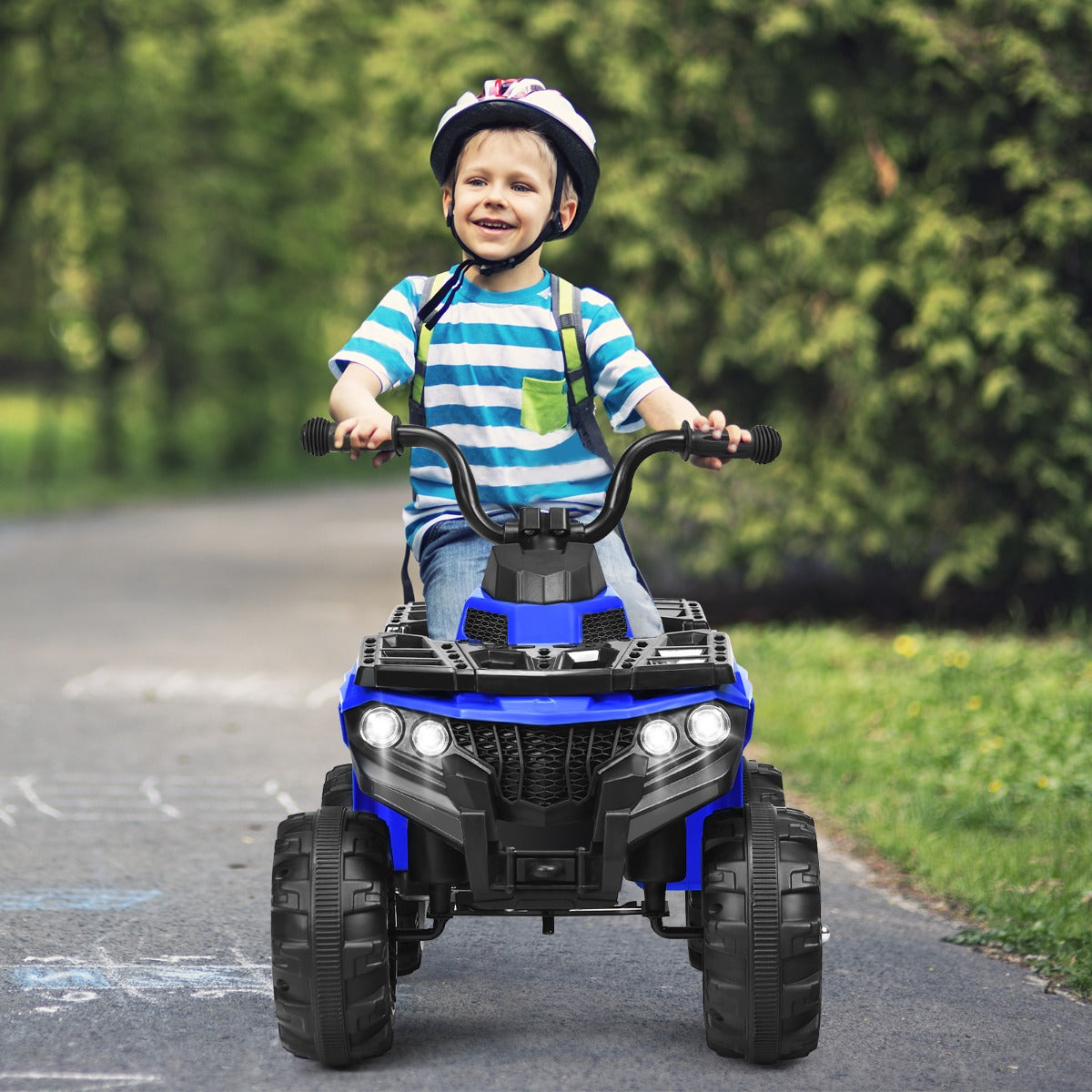 Front view of a happy boy riding the blue kids electric quad bike on a paved path