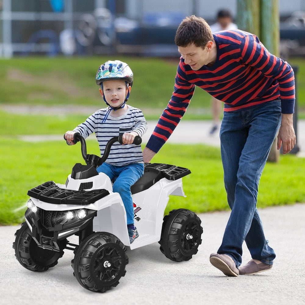 A young boy wearing a helmet rides the white kids electric quad bike while a man supervises