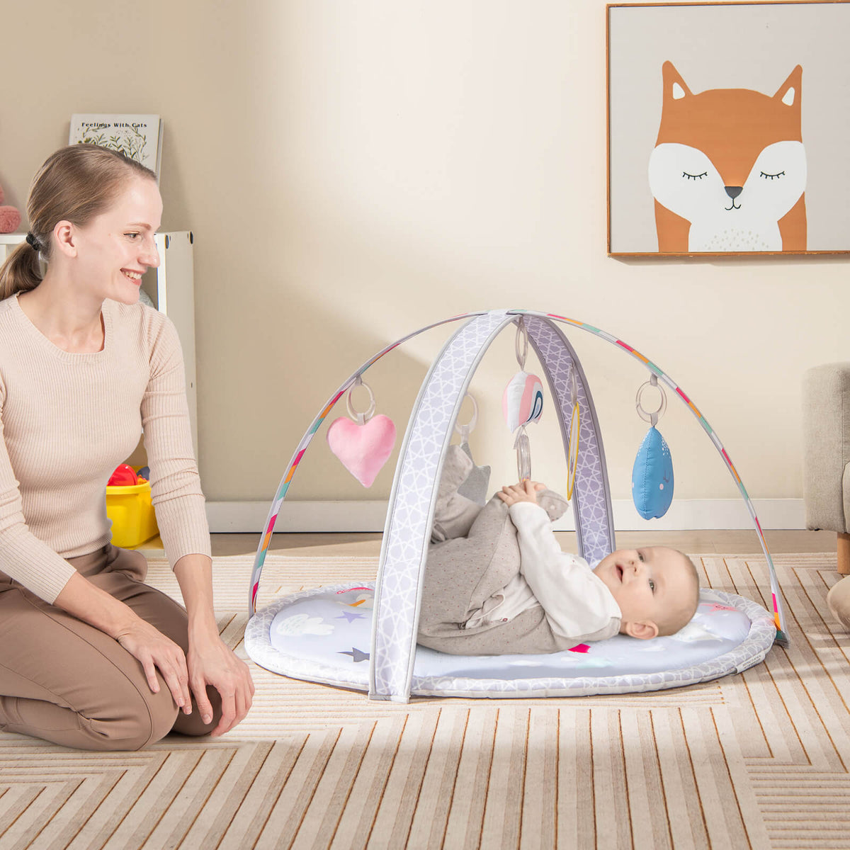 A mother plays with her baby on the baby play gym mat, which is set up on a carpeted floor
