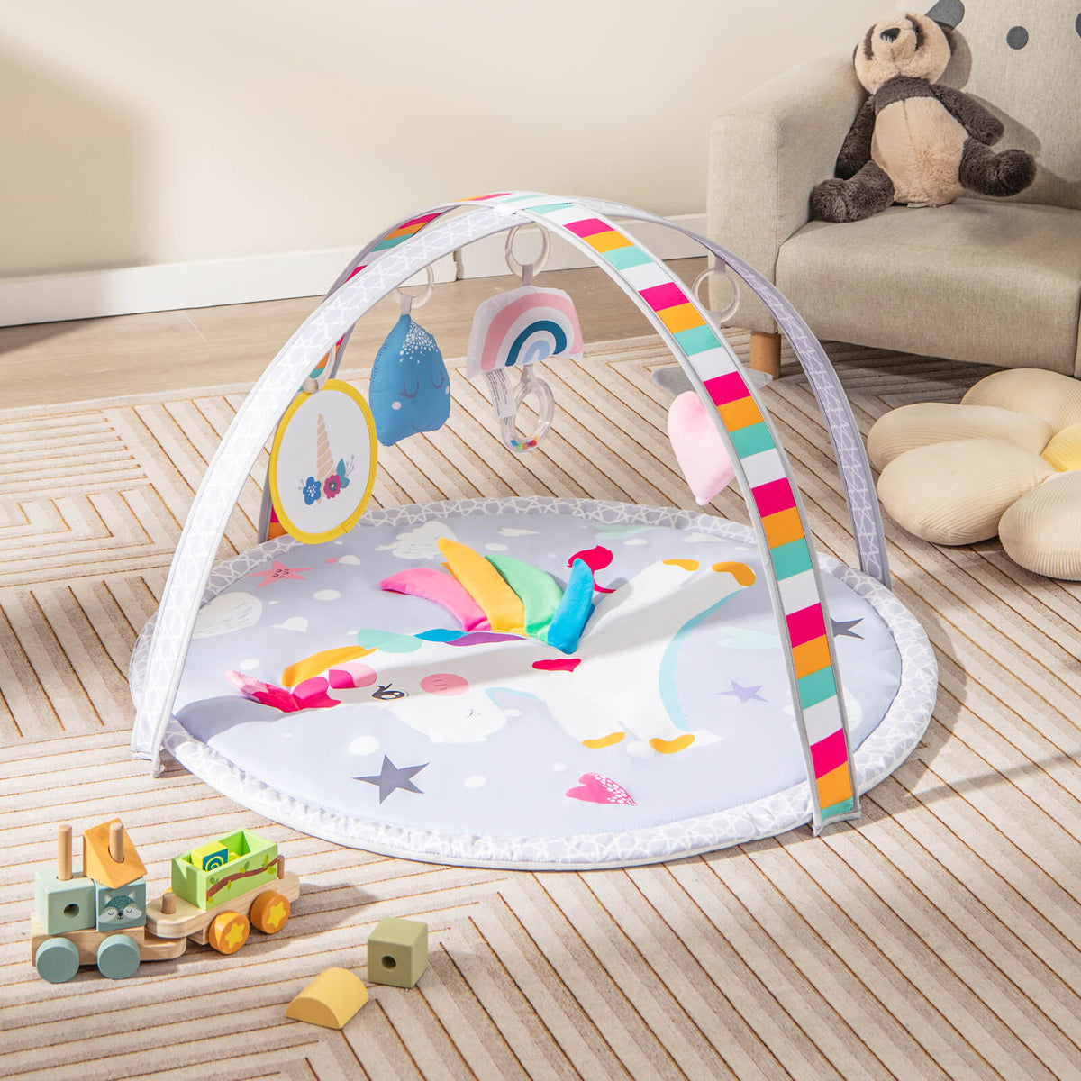 The baby play gym mat with arch and toys is set up on a wooden floor next to a sofa